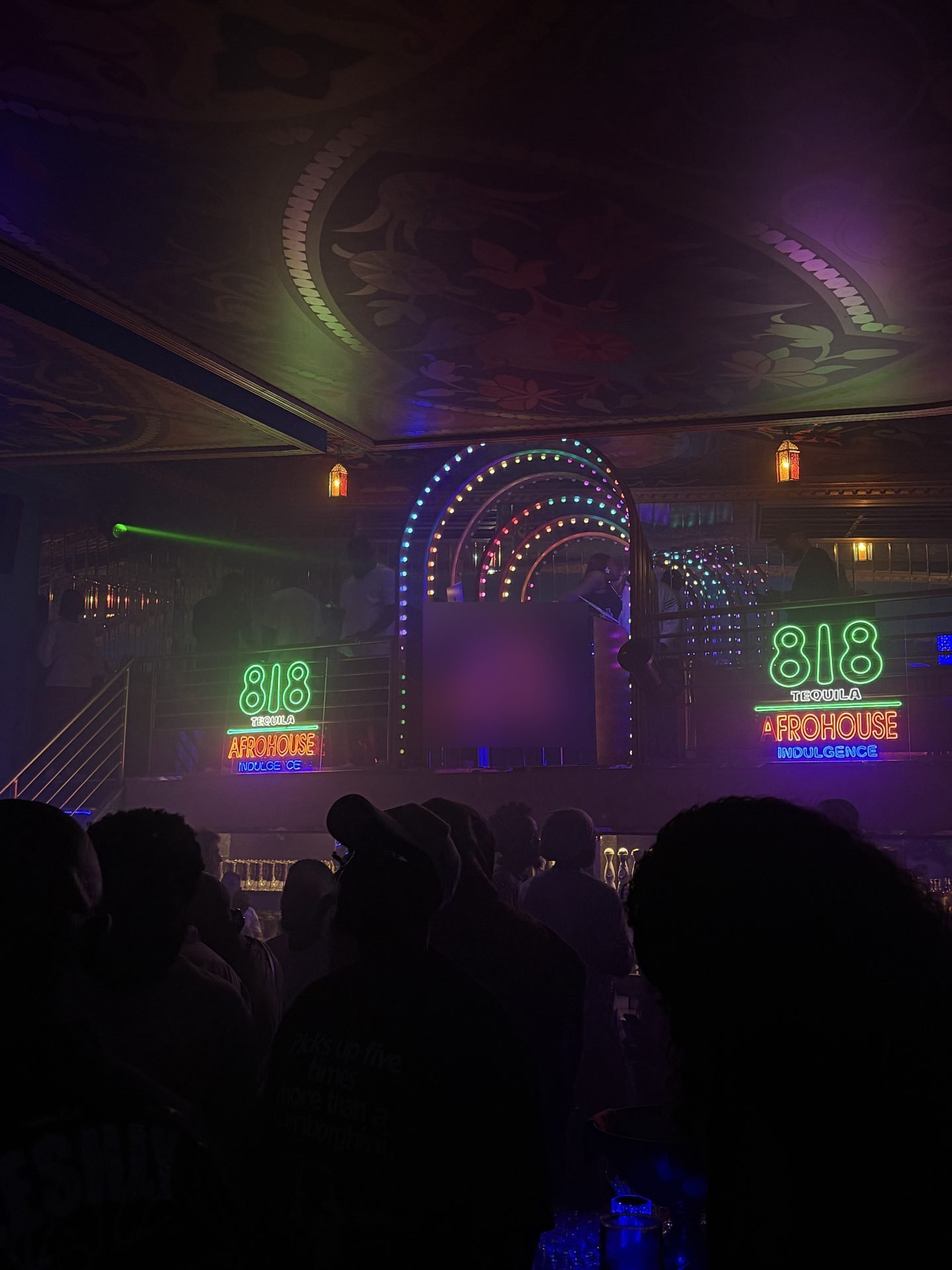 A packed Lagos club at night with colourful lights over the DJ booth