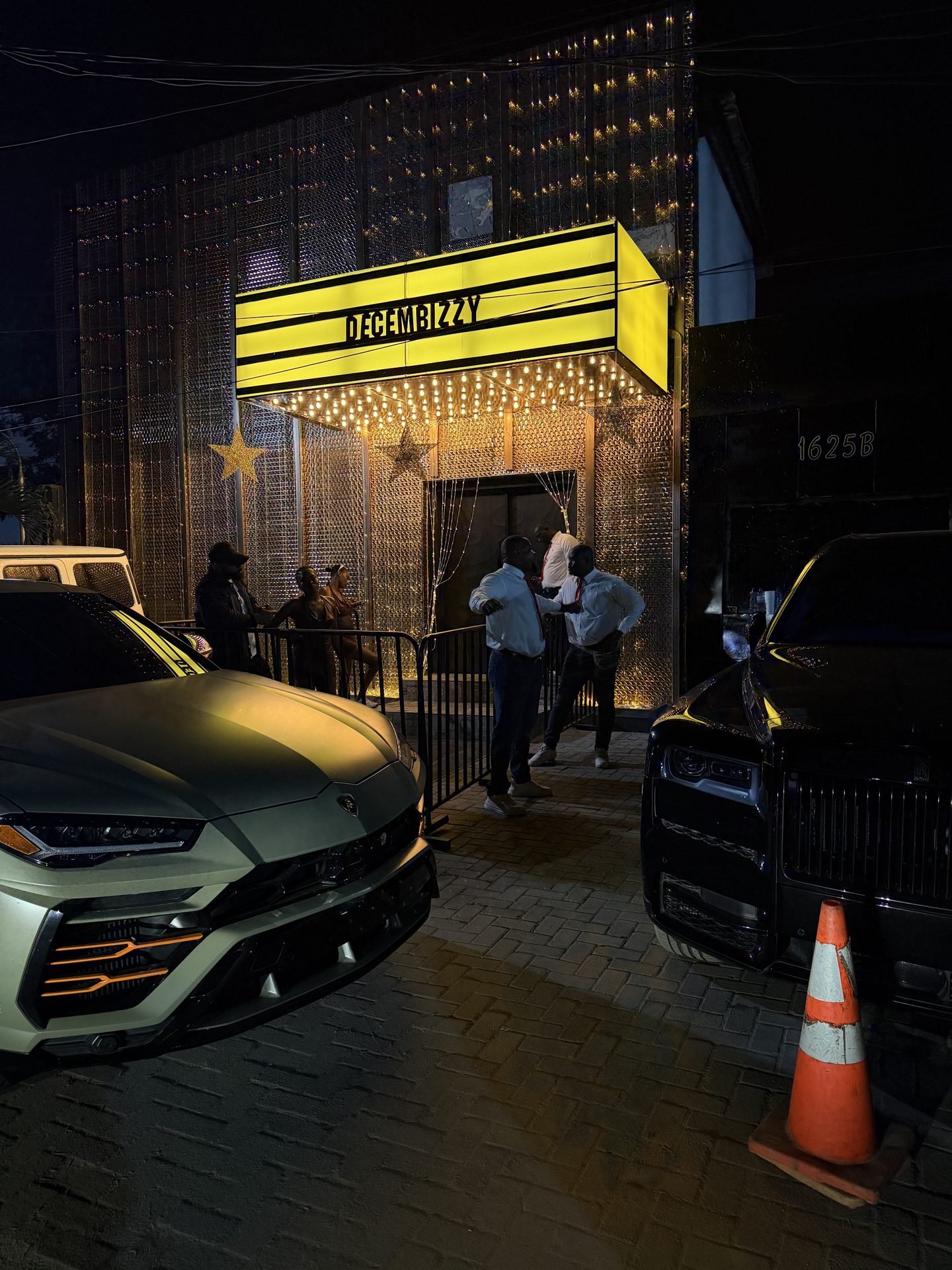 Luxury cars parked outside a lit-up December party venue
